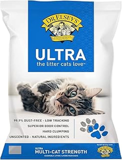 A cat is laying on a white surface with a bag of Dr. Elsey's Ultra UnScented Clumping Clay Cat Litter.